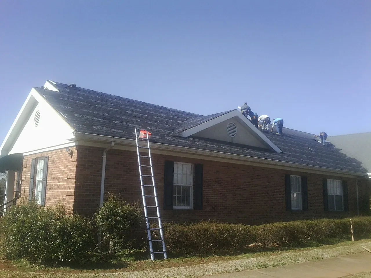 Crew tearing shingles off a brick ranch roof with a ladder set — Metal Roof Repair work by our crew in Mulberry
